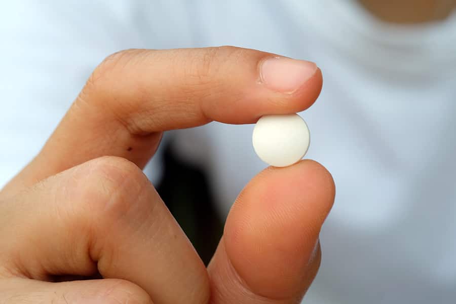 A hand holding a white pill